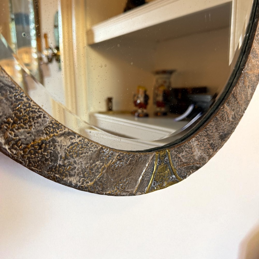 An oval Arts and Crafts wall mirror with a hand-hammered metal frame, decorative corner accents, and a bevelled mirror plate. View II