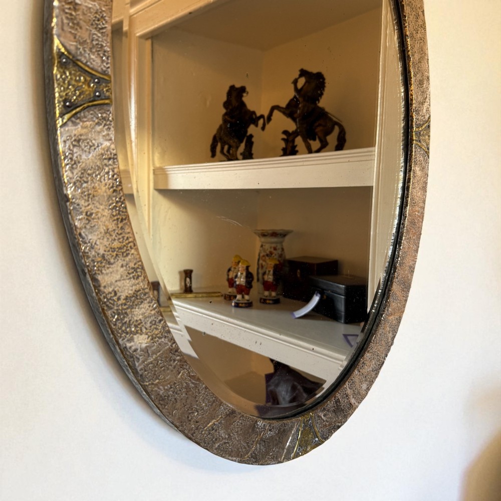 An oval Arts and Crafts wall mirror with a hand-hammered metal frame, decorative corner accents, and a bevelled mirror plate. View III