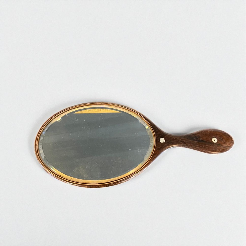 An oval antique rosewood hand mirror featuring mother-of-pearl inlay on the contoured handle and a bevelled glass plate.