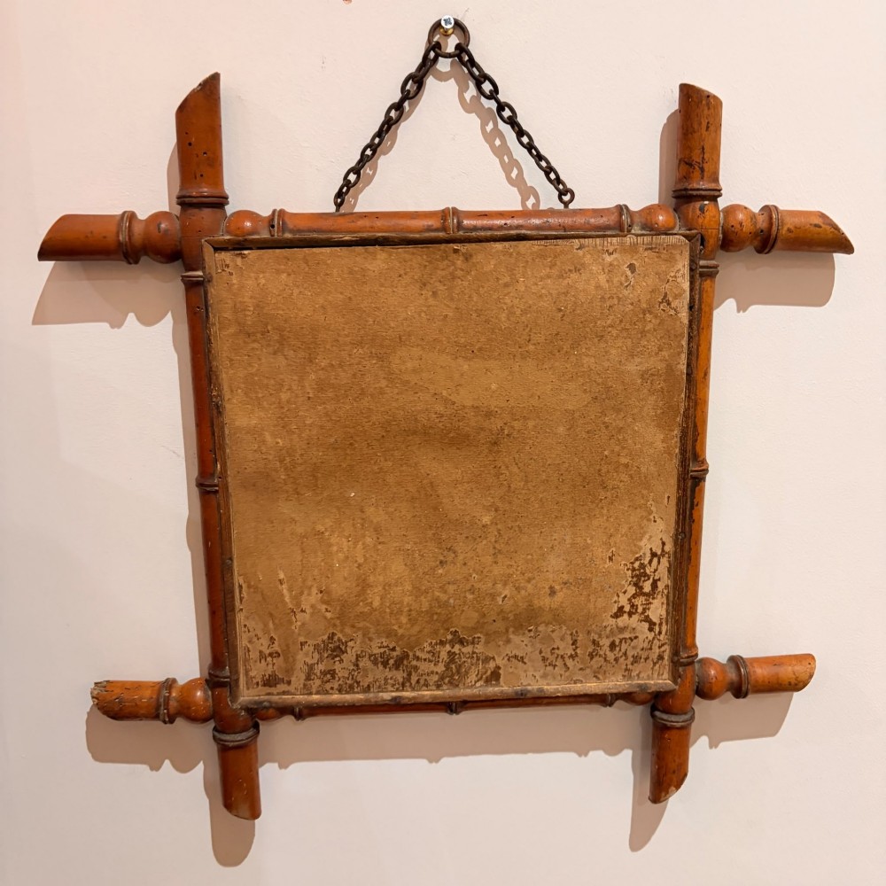 A square wall mirror framed in warm brown turned wood carved to resemble bamboo with extended corner joints and a metal suspension chain. View III