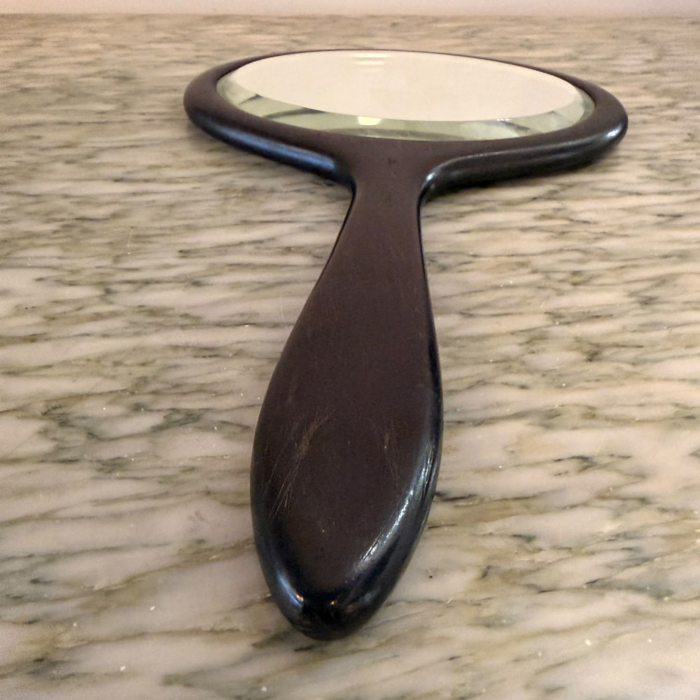 A Victorian oval ebony hand mirror featuring a bevelled glass mirror plate and a carved tapered handle. View II