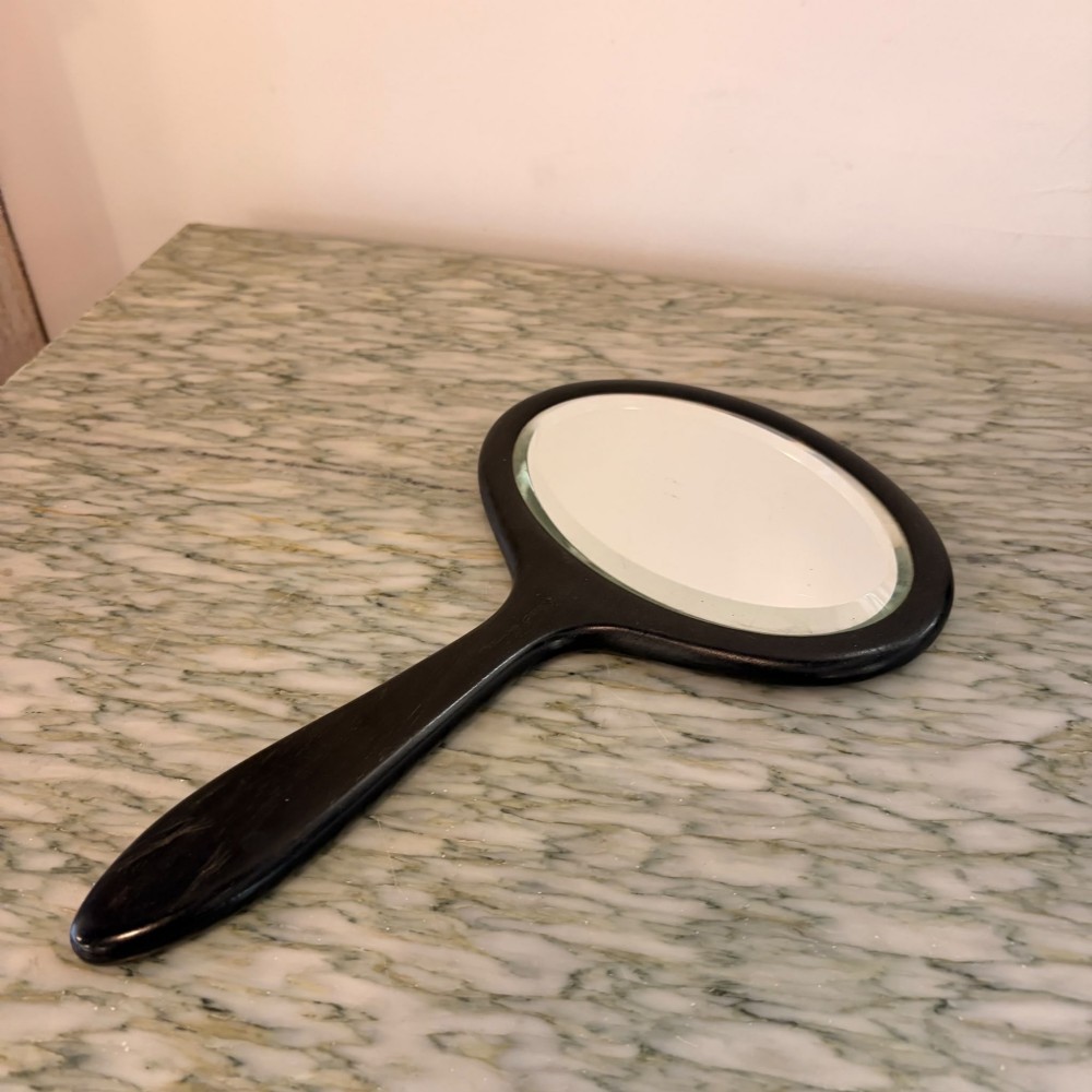 A Victorian oval ebony hand mirror featuring a bevelled glass mirror plate and a carved tapered handle.