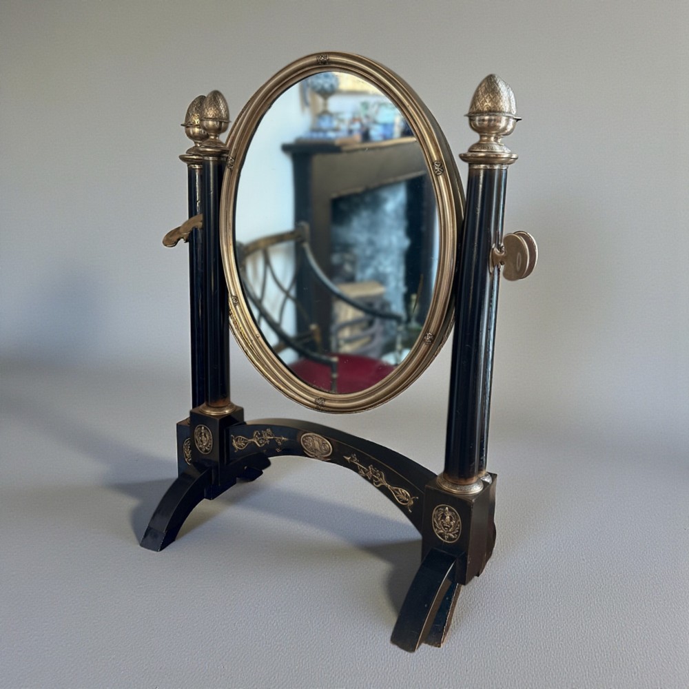 An antique 19th-century French ebonised toilet mirror featuring an oval glass frame suspended between twin columns with silvered finials and an arched base.