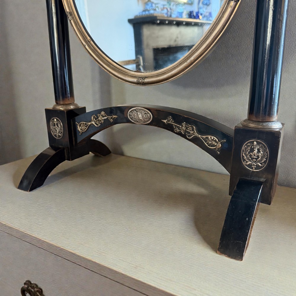 An antique 19th-century French ebonised toilet mirror featuring an oval glass frame suspended between twin columns with silvered finials and an arched base. View II