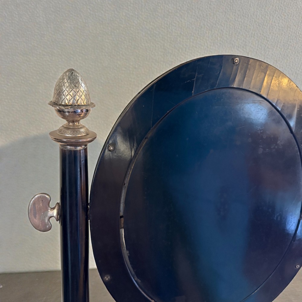 An antique 19th-century French ebonised toilet mirror featuring an oval glass frame suspended between twin columns with silvered finials and an arched base. View V