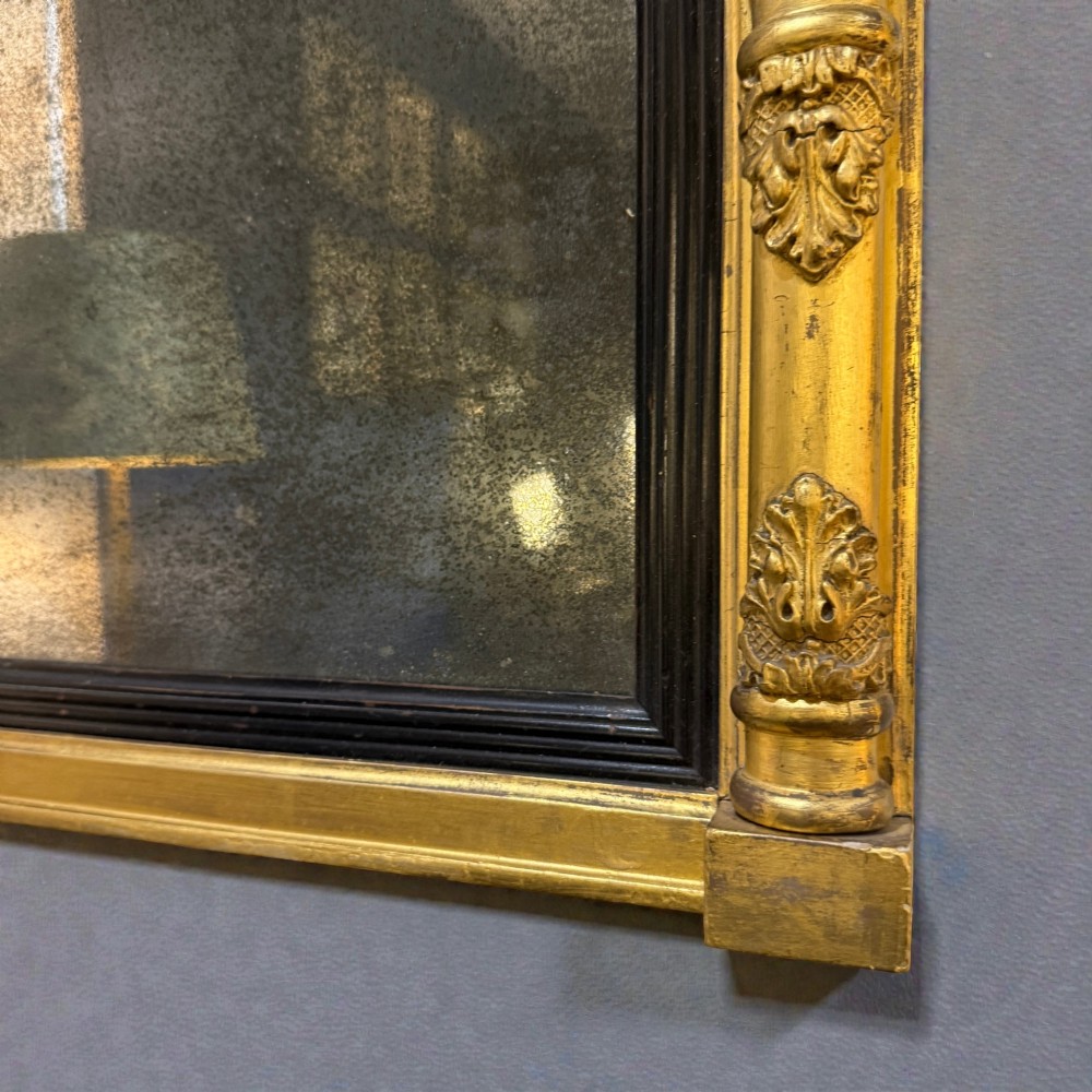 A 19th-century giltwood wall mirror featuring an architectural breakfront cornice, acanthus leaf carved column pilasters, an ebonised inner slip, and foxed mirror glass. View II