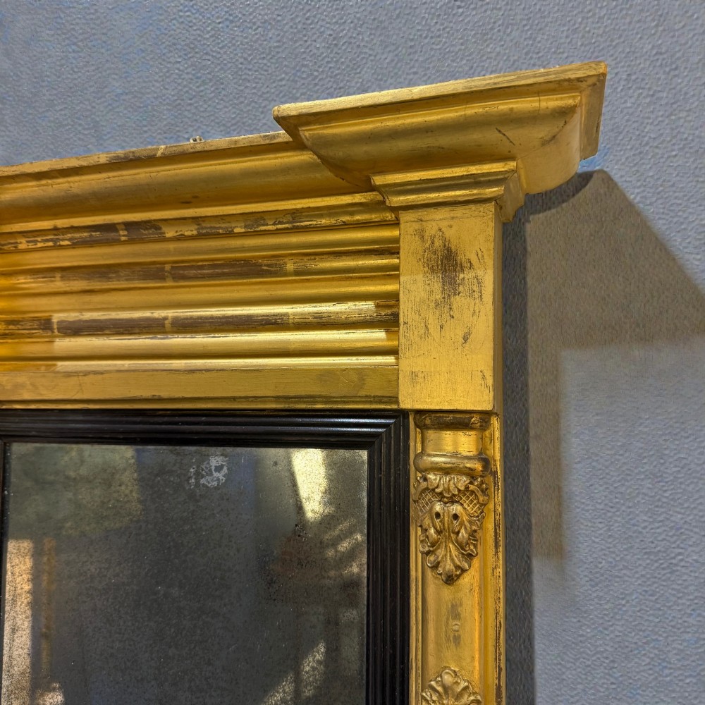 A 19th-century giltwood wall mirror featuring an architectural breakfront cornice, acanthus leaf carved column pilasters, an ebonised inner slip, and foxed mirror glass. View III