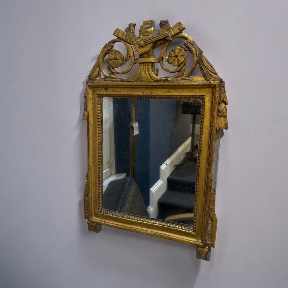 An early nineteenth-century rectangular giltwood wall mirror featuring an intricate carved cresting with a musical instrument motif and a beaded inner border.