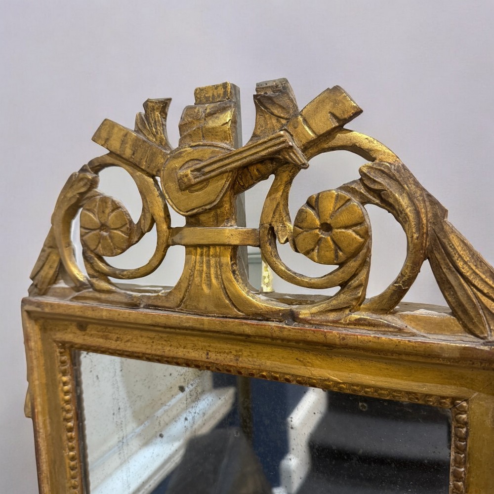 An early nineteenth-century rectangular giltwood wall mirror featuring an intricate carved cresting with a musical instrument motif and a beaded inner border. View II