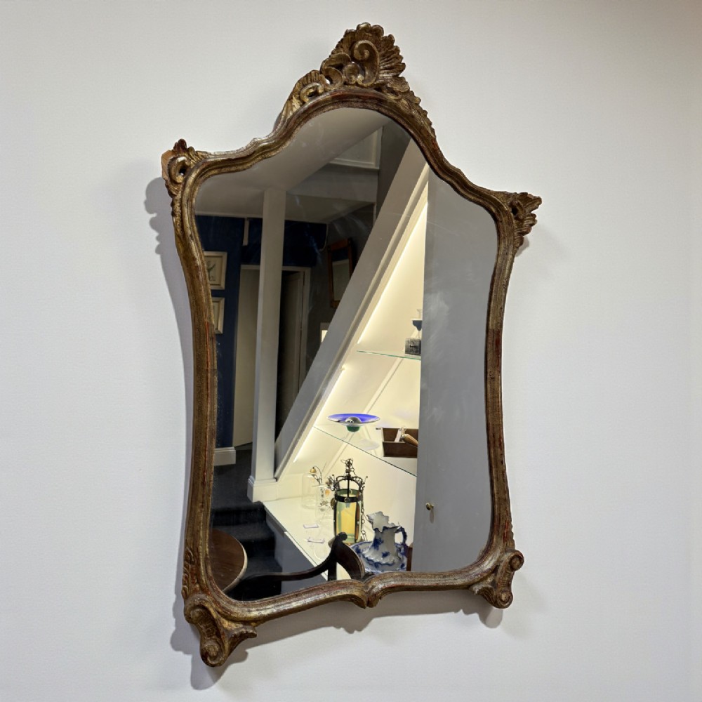 A late 19th-century French Rococo revival wall mirror featuring an ornate carved gold giltwood frame with scroll cresting and a shaped glass plate.