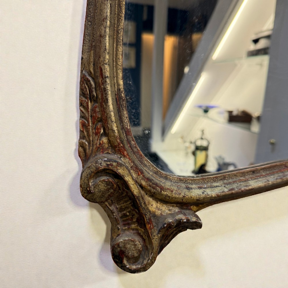 A late 19th-century French Rococo revival wall mirror featuring an ornate carved gold giltwood frame with scroll cresting and a shaped glass plate. View II