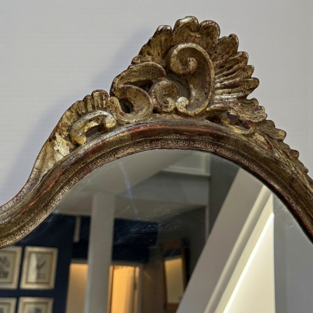 A late 19th-century French Rococo revival wall mirror featuring an ornate carved gold giltwood frame with scroll cresting and a shaped glass plate. View III
