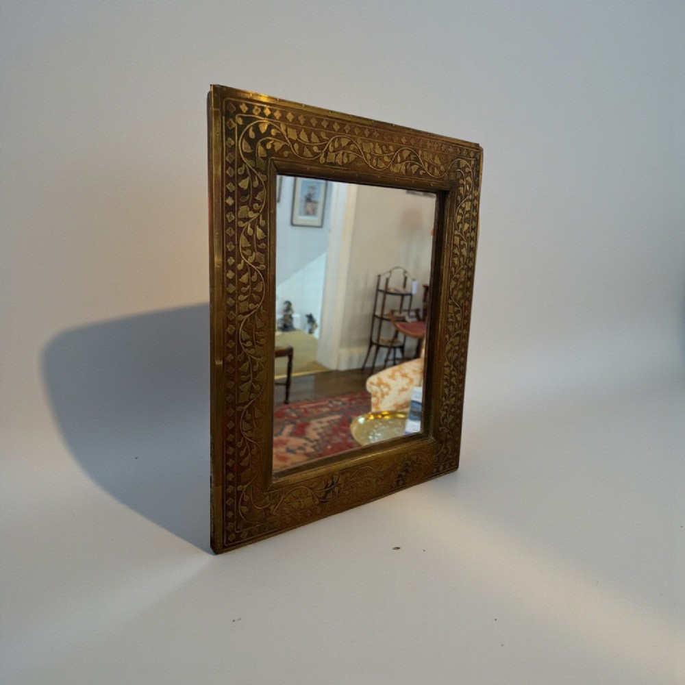 A square wooden mirror featuring intricate brass floral wire inlay along its wide rectangular border. View II