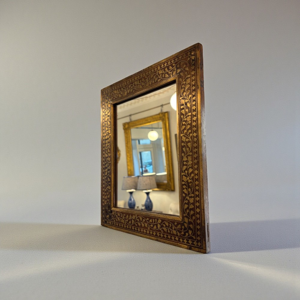 A square wooden mirror featuring intricate brass floral wire inlay along its wide rectangular border.
