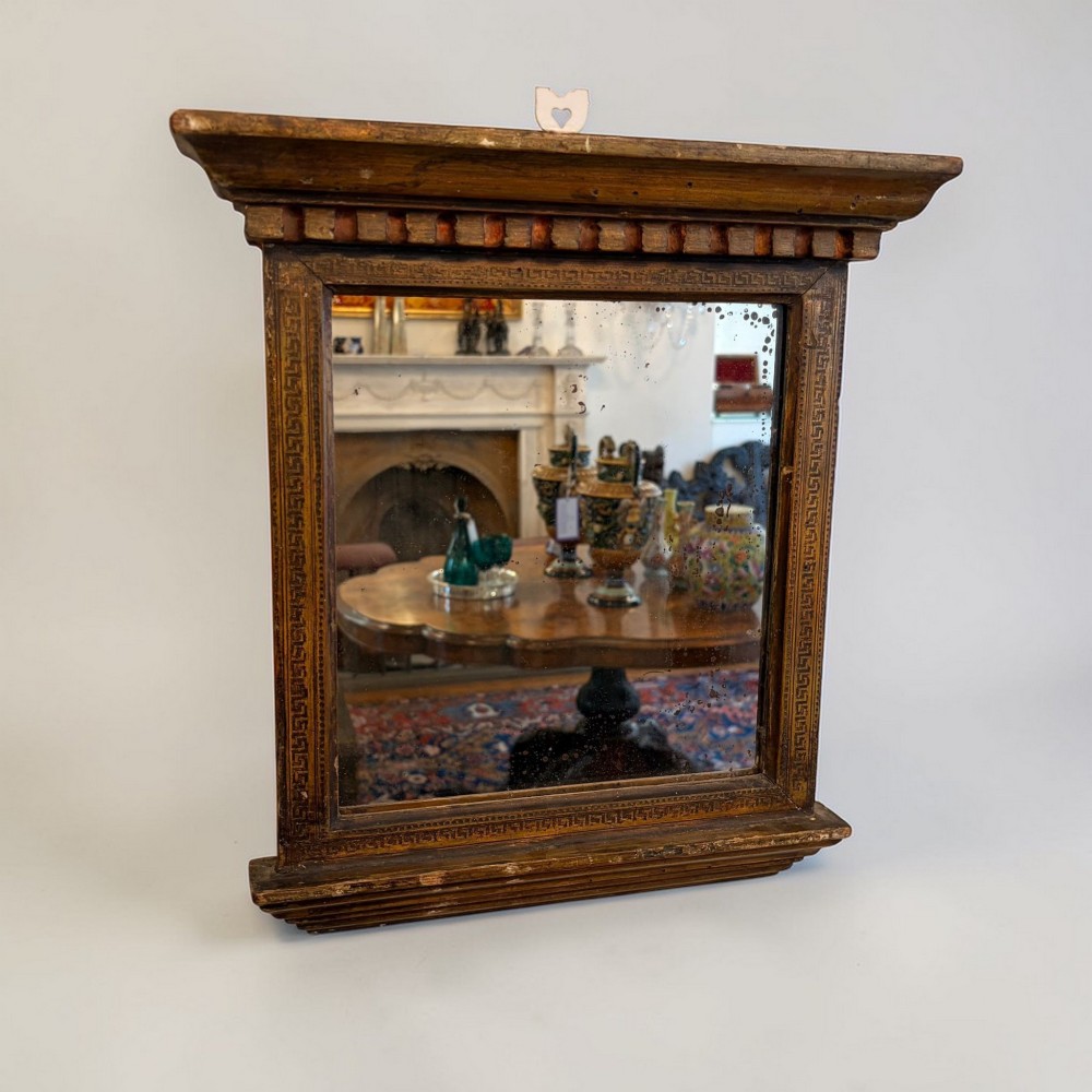 A nineteenth-century Neoclassical rectangular wall mirror featuring an architectural cornice, dentil moulding, carved Greek key border details, and foxed glass.