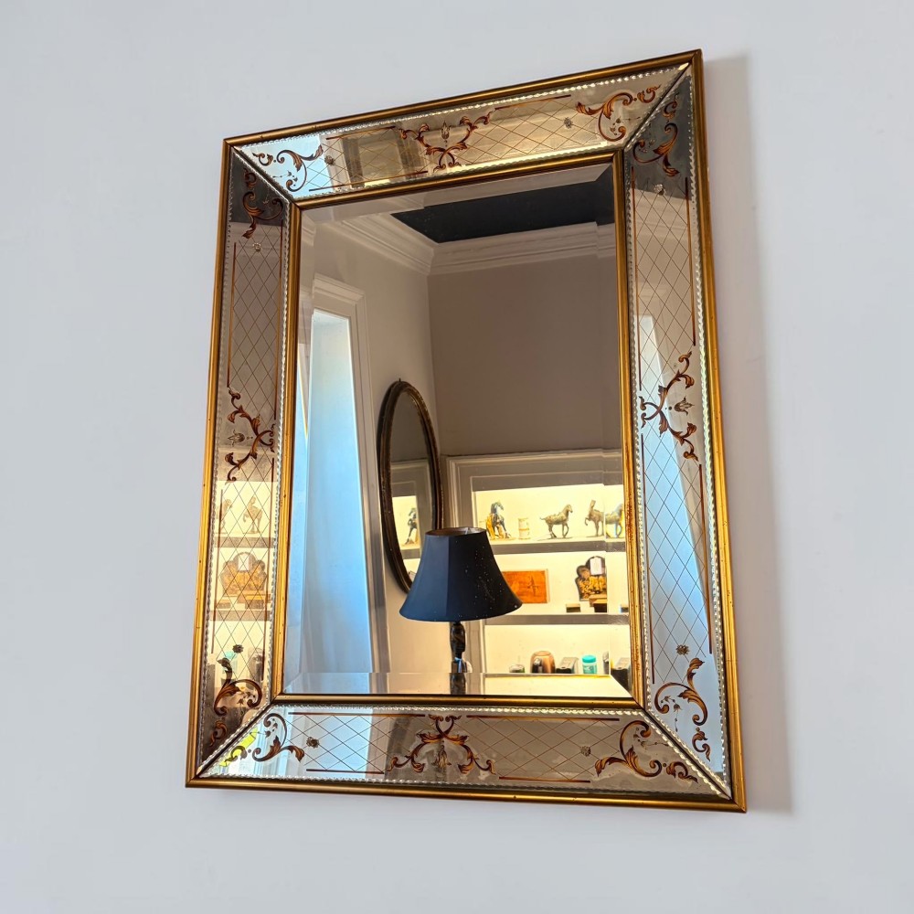 A rectangular Venetian style mirror featuring a central bevelled mirror plate surrounded by mirrored borders with gold scrollwork and diamond lattice etching.