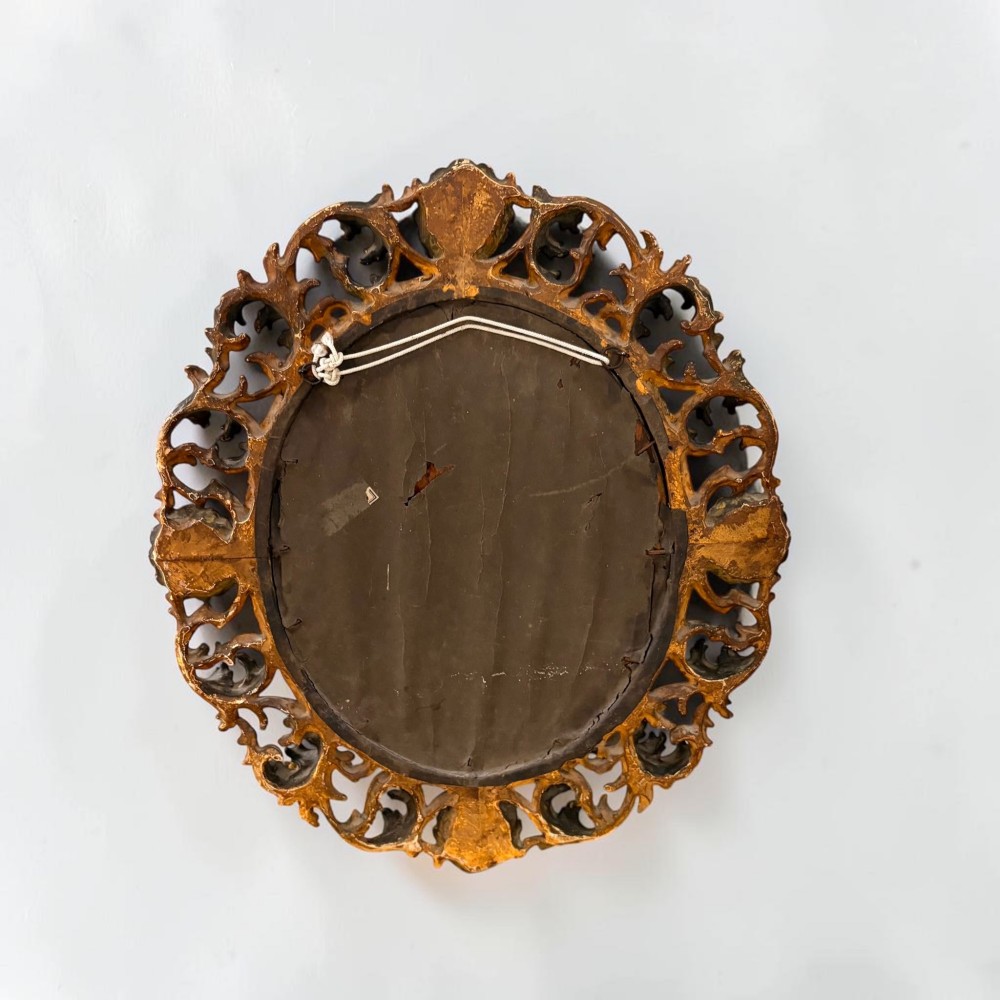 An oval mirror surrounded by an ornate gold gilt Florentine frame featuring carved acanthus leaf scrollwork and shell motifs. View III