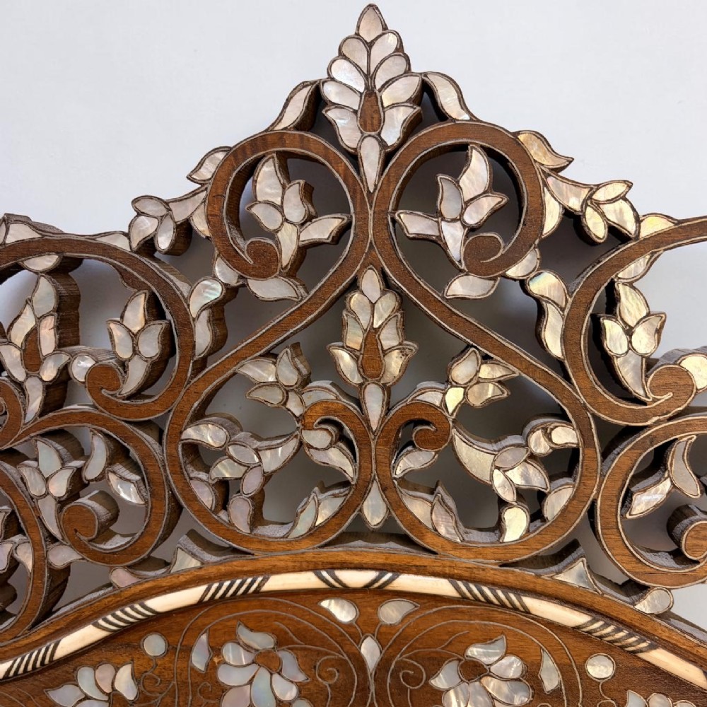A Syrian wall mirror featuring a shaped dark wood frame with detailed mother-of-pearl floral inlays and an openwork pierced cresting. View II