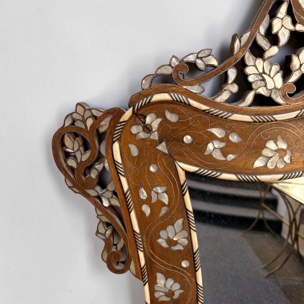 A Syrian wall mirror featuring a shaped dark wood frame with detailed mother-of-pearl floral inlays and an openwork pierced cresting. View III