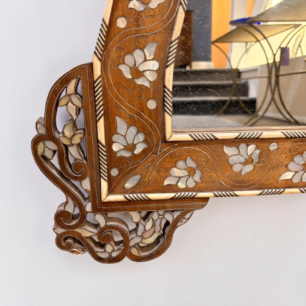 A Syrian wall mirror featuring a shaped dark wood frame with detailed mother-of-pearl floral inlays and an openwork pierced cresting. View IV