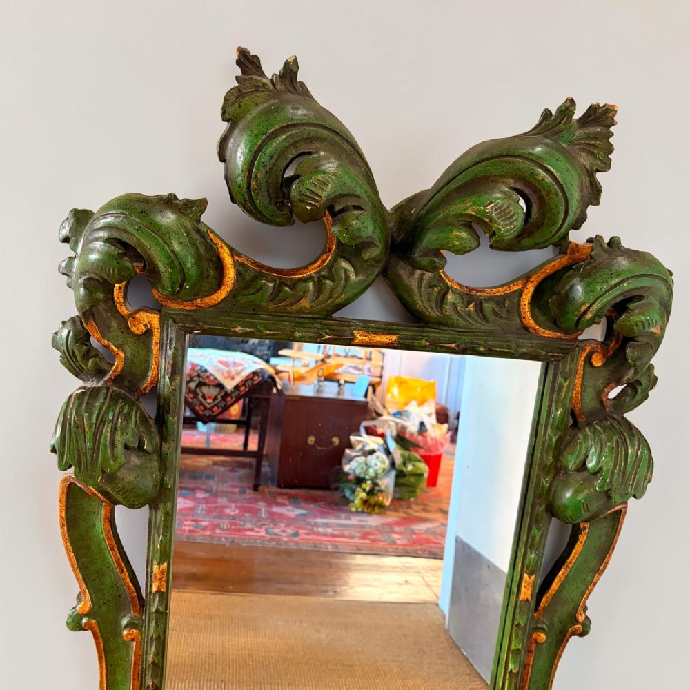 An ornate Italian Florentine style carved wooden mirror painted in olive green with gold leaf accents along scrolled acanthus leaf borders. View II