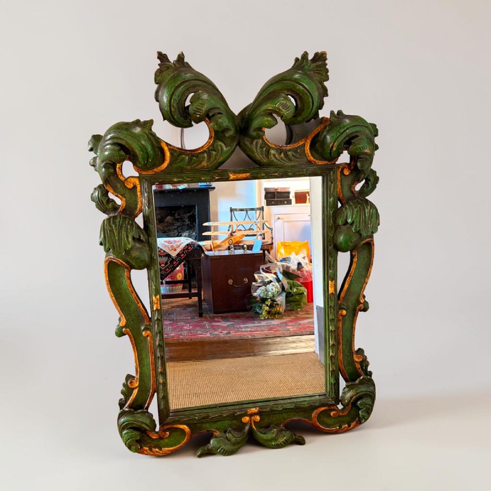 An ornate Italian Florentine style carved wooden mirror painted in olive green with gold leaf accents along scrolled acanthus leaf borders.