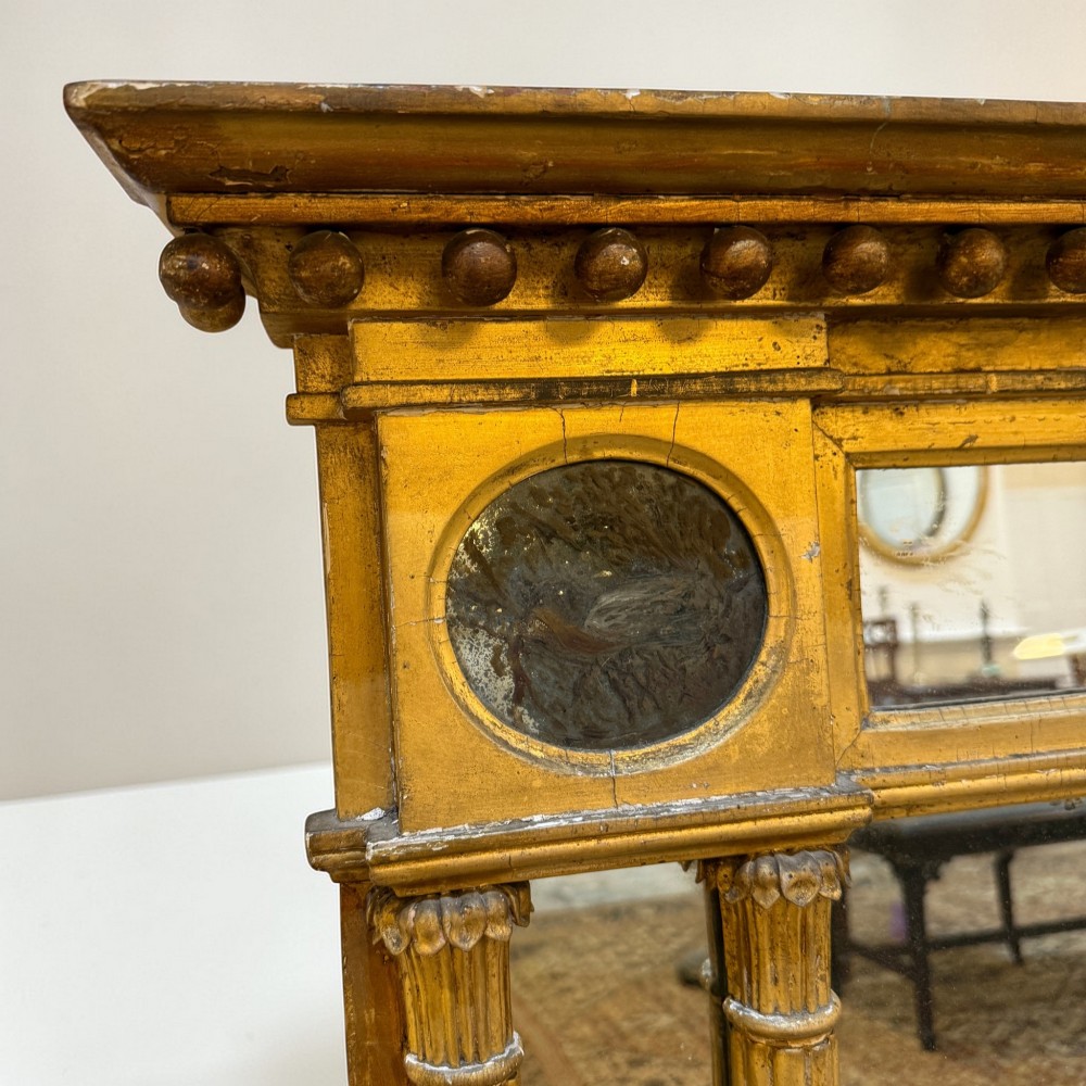 A Regency giltwood overmantel mirror featuring a breakfront cornice with spherules, fluted pilasters, corner roundels, and a three-plate glass design. View II