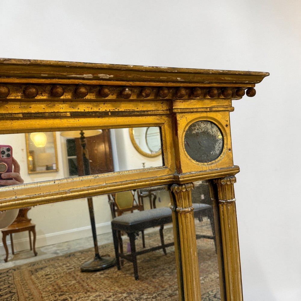 A Regency giltwood overmantel mirror featuring a breakfront cornice with spherules, fluted pilasters, corner roundels, and a three-plate glass design. View III