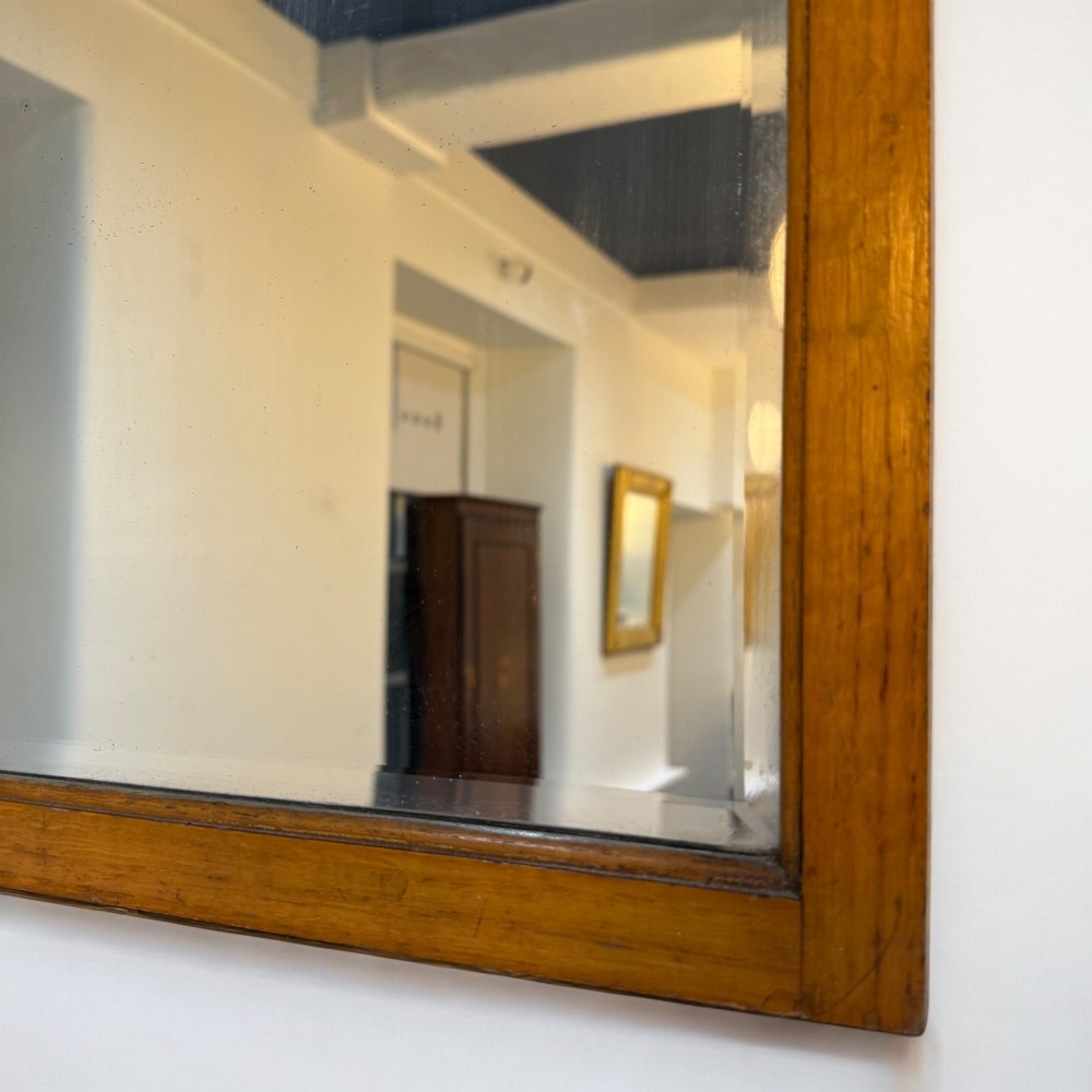 An upright rectangular wall mirror with a warm oak wooden frame and a shaped arched crest at the top. View II