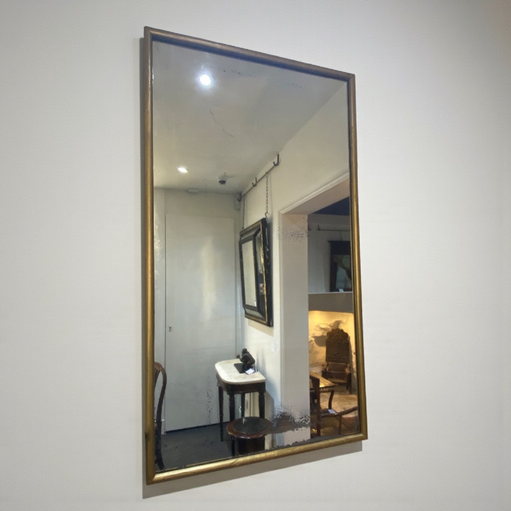 A tall rectangular 19th-century French Neoclassical wall mirror featuring a narrow gilded wooden frame and aged mirror glass.
