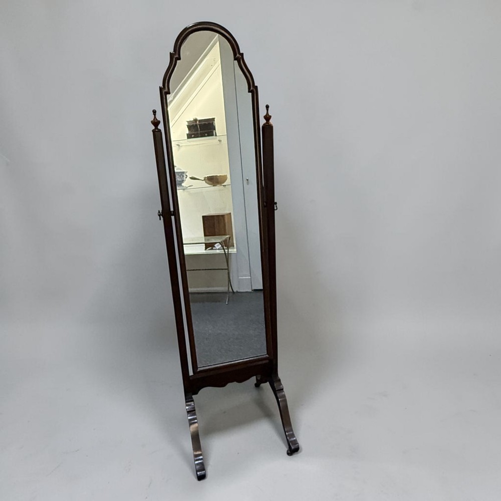 An Edwardian mahogany cheval dressing mirror featuring an arched top frame, turning brass pivots, and splayed sabre legs.