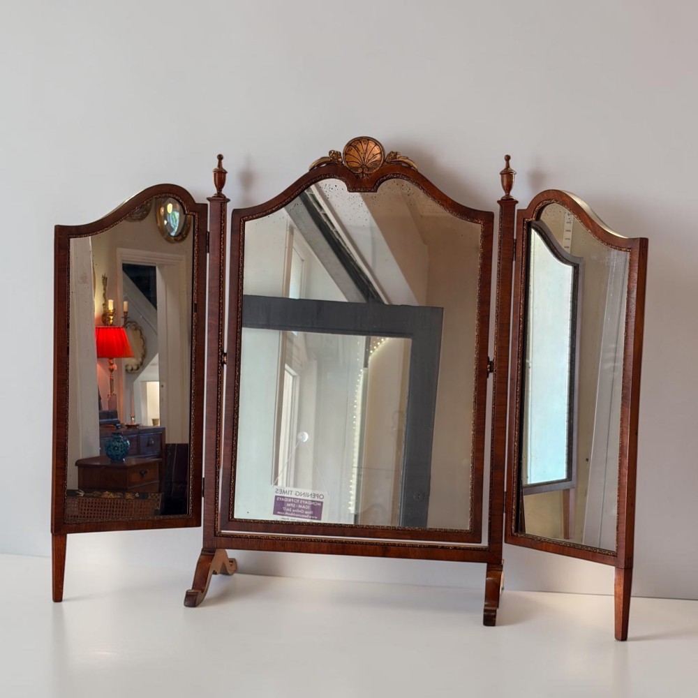 An Edwardian mahogany tri-fold dressing mirror featuring an arched central frame with a carved shell cresting and adjustable side panels.