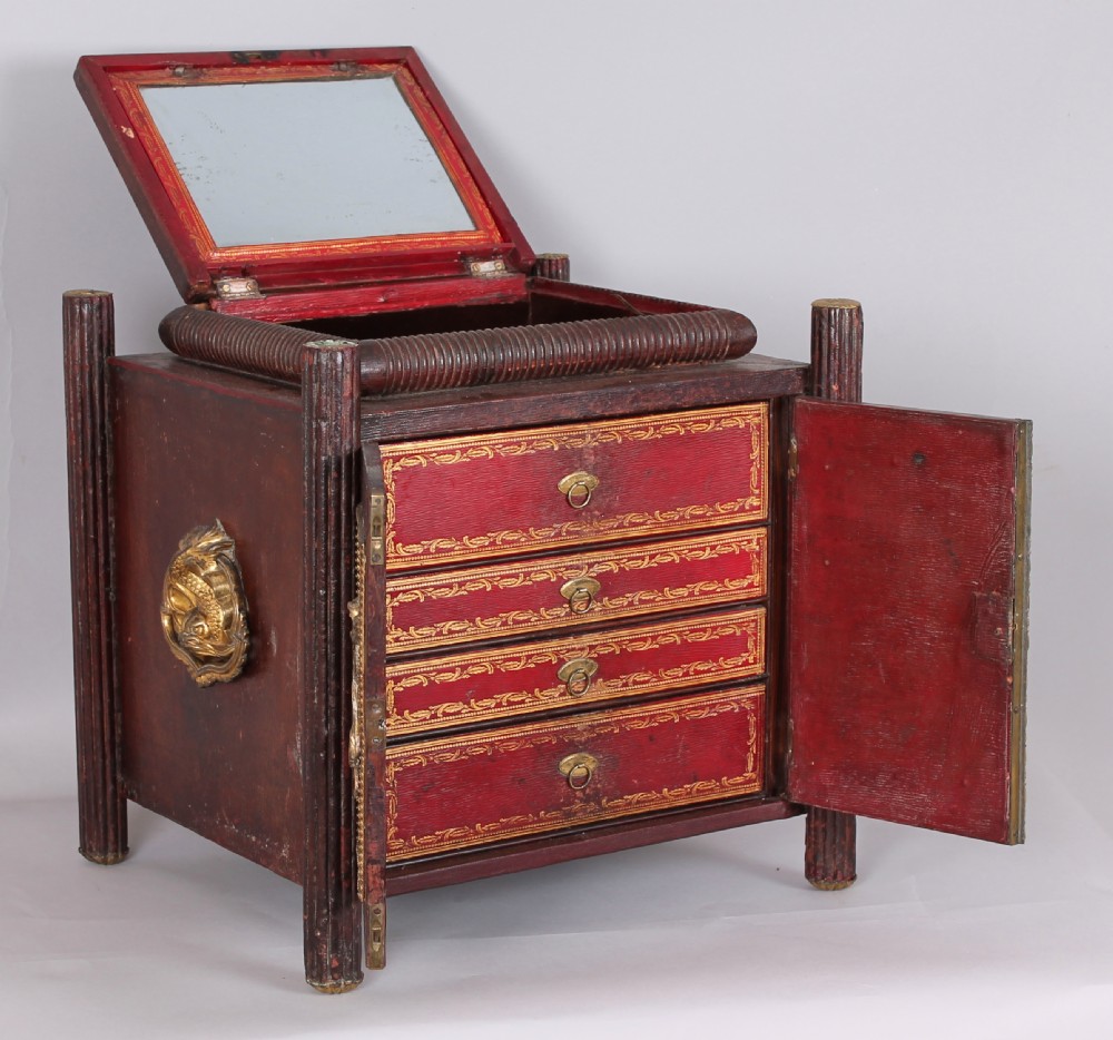 An early nineteenth-century table-cabinet bound in deep red tooled leather, featuring fluted column corner posts, classical gilt-brass figure mounts on the twin doors, and dolphin side handles. View II