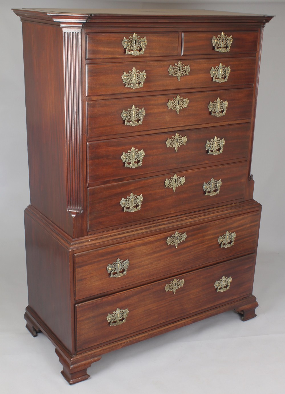 A George II mahogany chest on chest featuring reeded canted corners, pierced brass handles, and bracket feet.