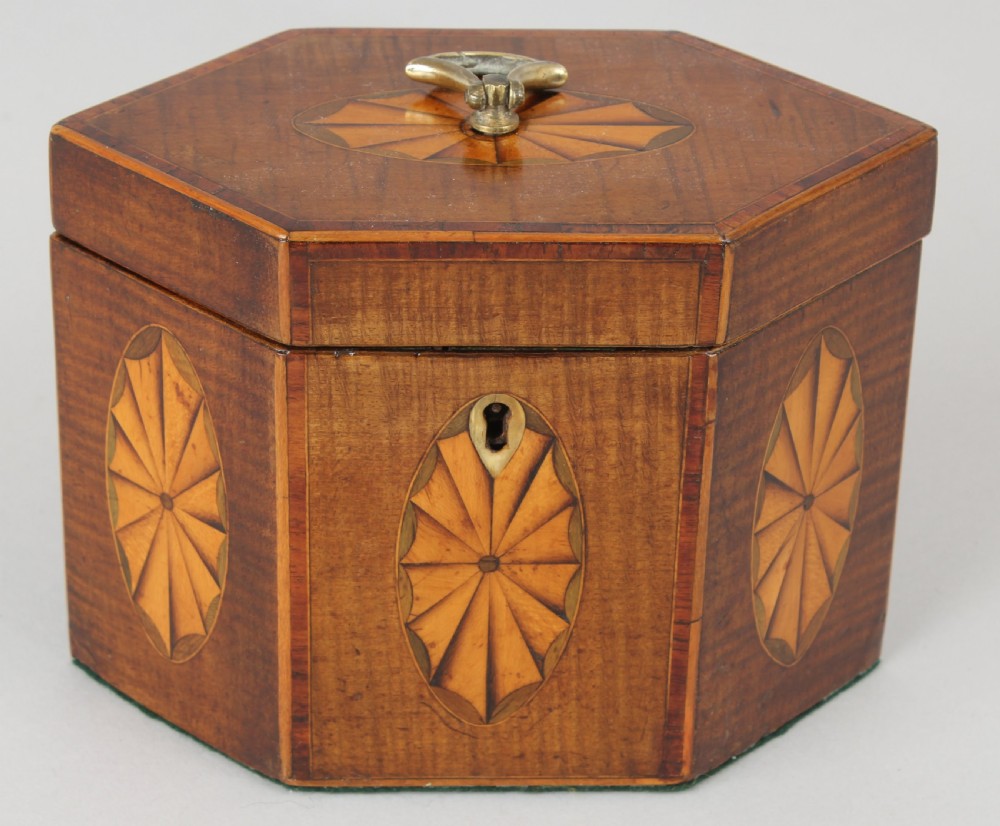 A George III hexagonal harewood tea caddy featuring oval fan marquetry motifs on its sides and top lid with a brass loop handle.