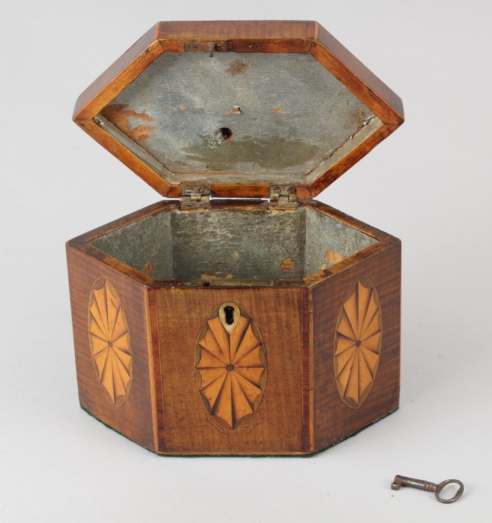 A George III hexagonal harewood tea caddy featuring oval fan marquetry motifs on its sides and top lid with a brass loop handle. View III