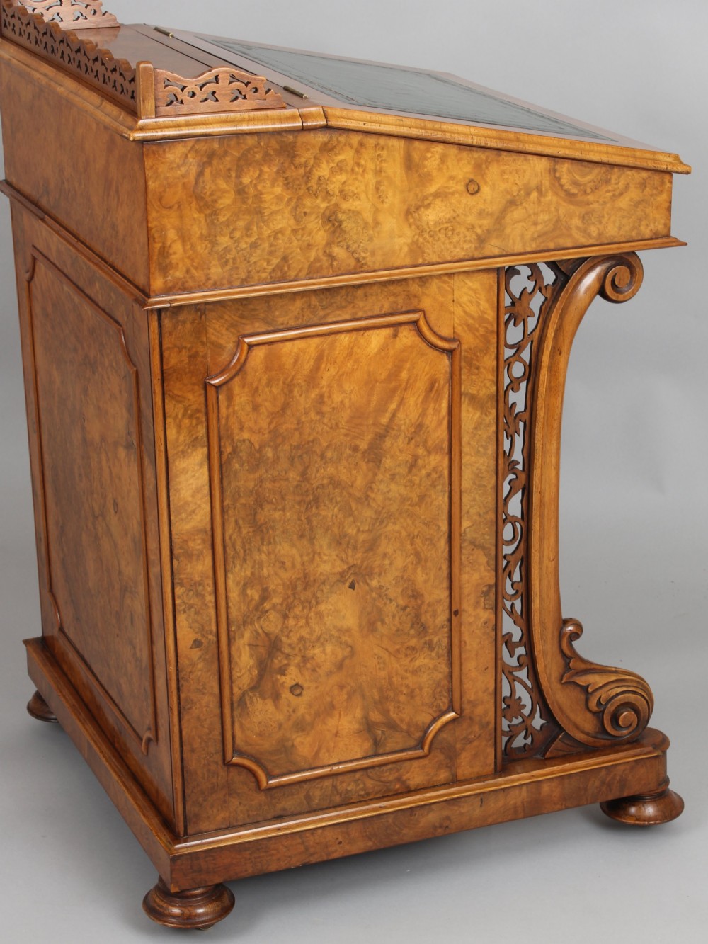 A Victorian burr walnut Davenport desk featuring a sloped green leather writing top, carved fretwork gallery, and side cabinet door on brass castors. View II