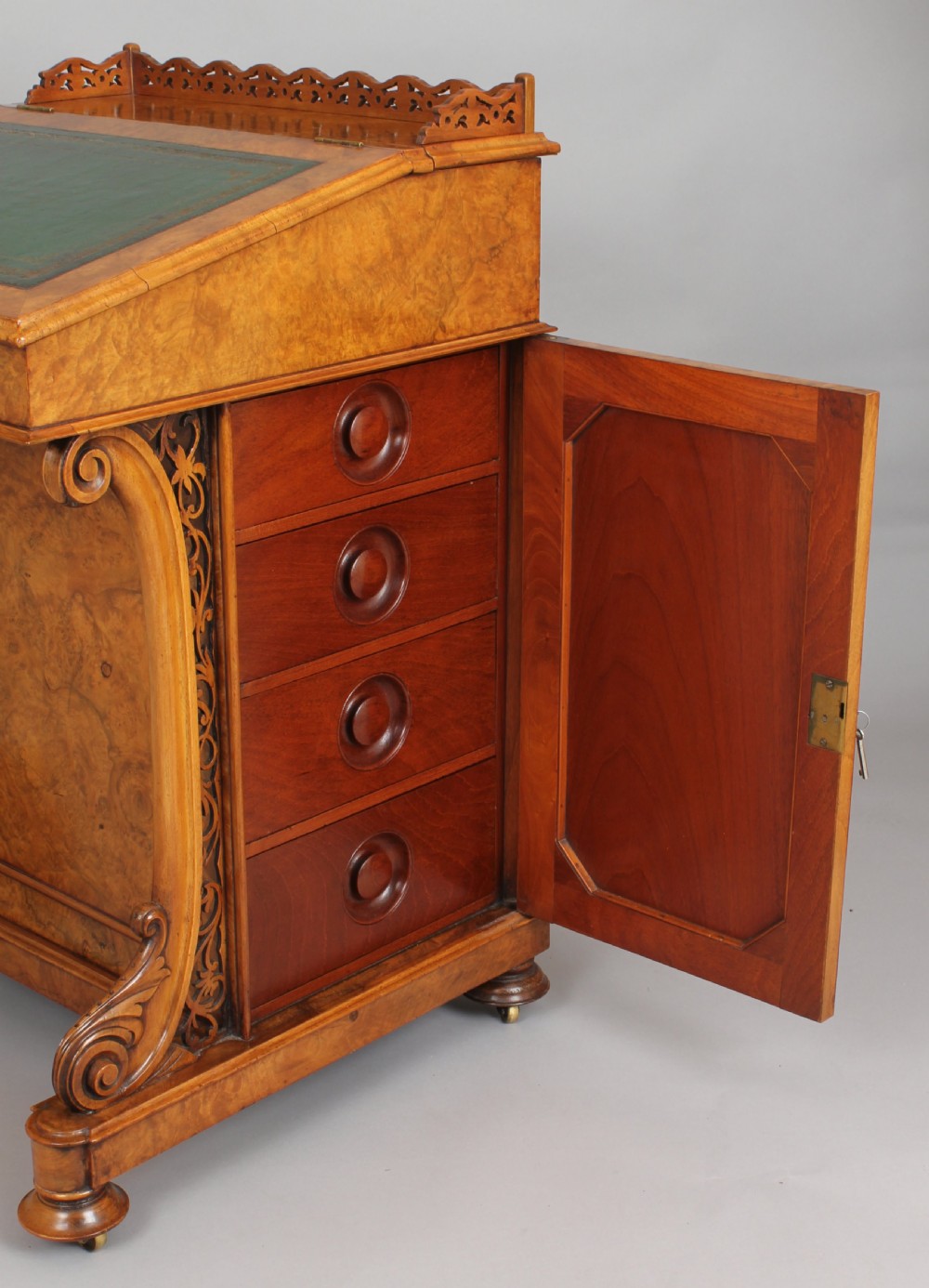 A Victorian burr walnut Davenport desk featuring a sloped green leather writing top, carved fretwork gallery, and side cabinet door on brass castors. View III