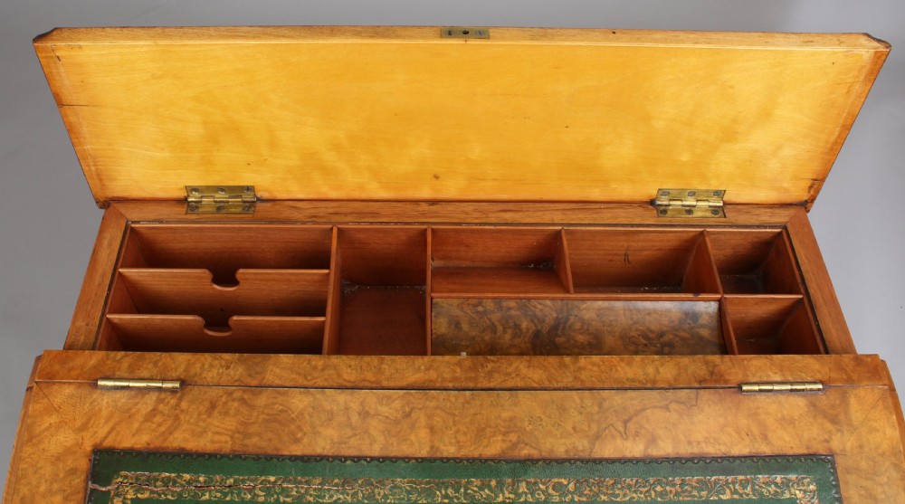 A Victorian burr walnut Davenport desk featuring a sloped green leather writing top, carved fretwork gallery, and side cabinet door on brass castors. View IV