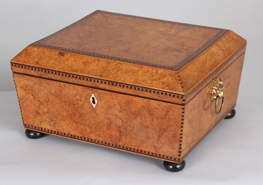 A Regency period sarcophagus-shaped work box crafted from golden birdseye maple with geometric ebony inlay, brass lion mask ring handles, and ball feet. View II