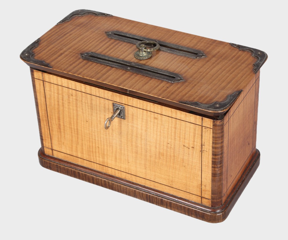 A rectangular 19th-century French wooden box with figured timber veneer, dual lid slots, central brass ring handle, metal corner mounts, and a key inserted in the front lock.