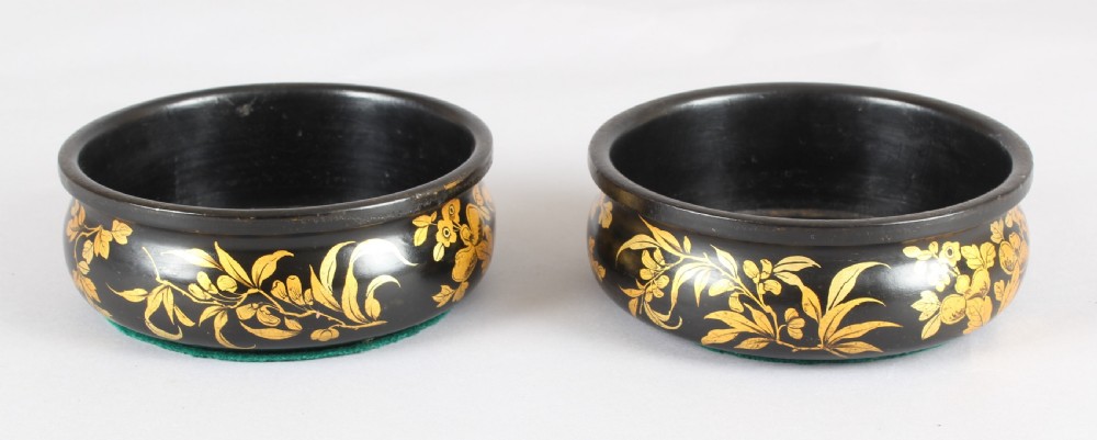 A pair of circular Victorian black lacquer papier-mache bottle coasters featuring hand-painted gold floral foliage.