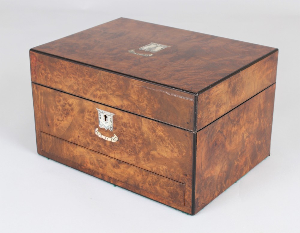 A rectangular Victorian burr walnut dressing box featuring a lockable lid, silver escutcheon, and inlaid top cartouche against a plain background.