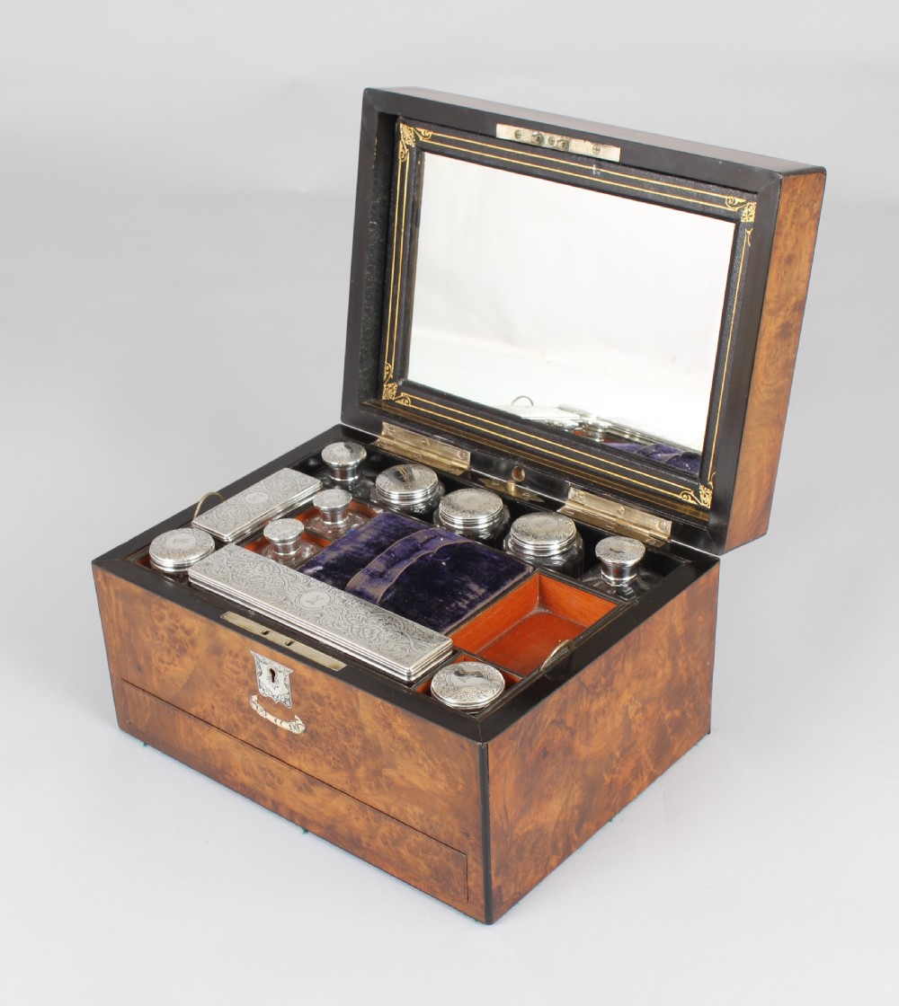 A rectangular Victorian burr walnut dressing box featuring a lockable lid, silver escutcheon, and inlaid top cartouche against a plain background. View V