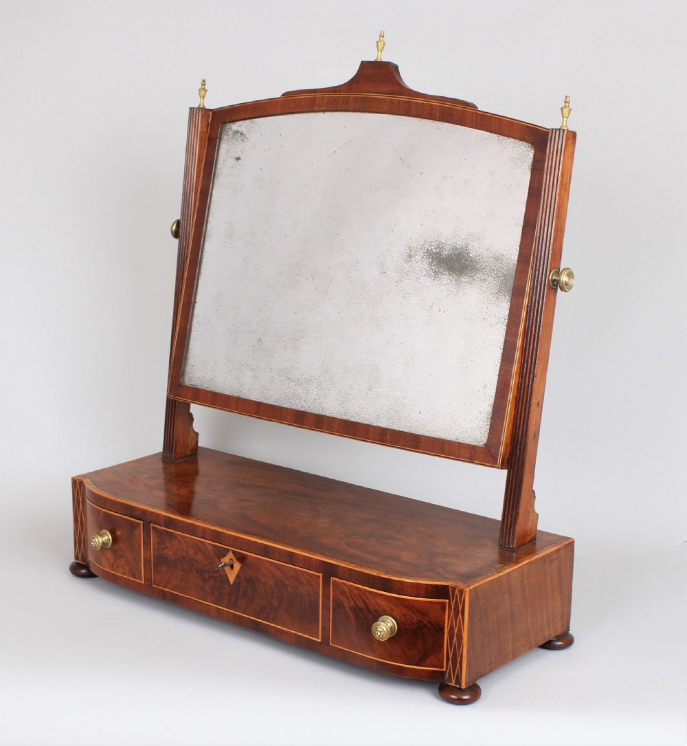 A George IV mahogany toilet mirror featuring an adjustable rectangular glass plate supported by fluted uprights over a bow-fronted drawer base.