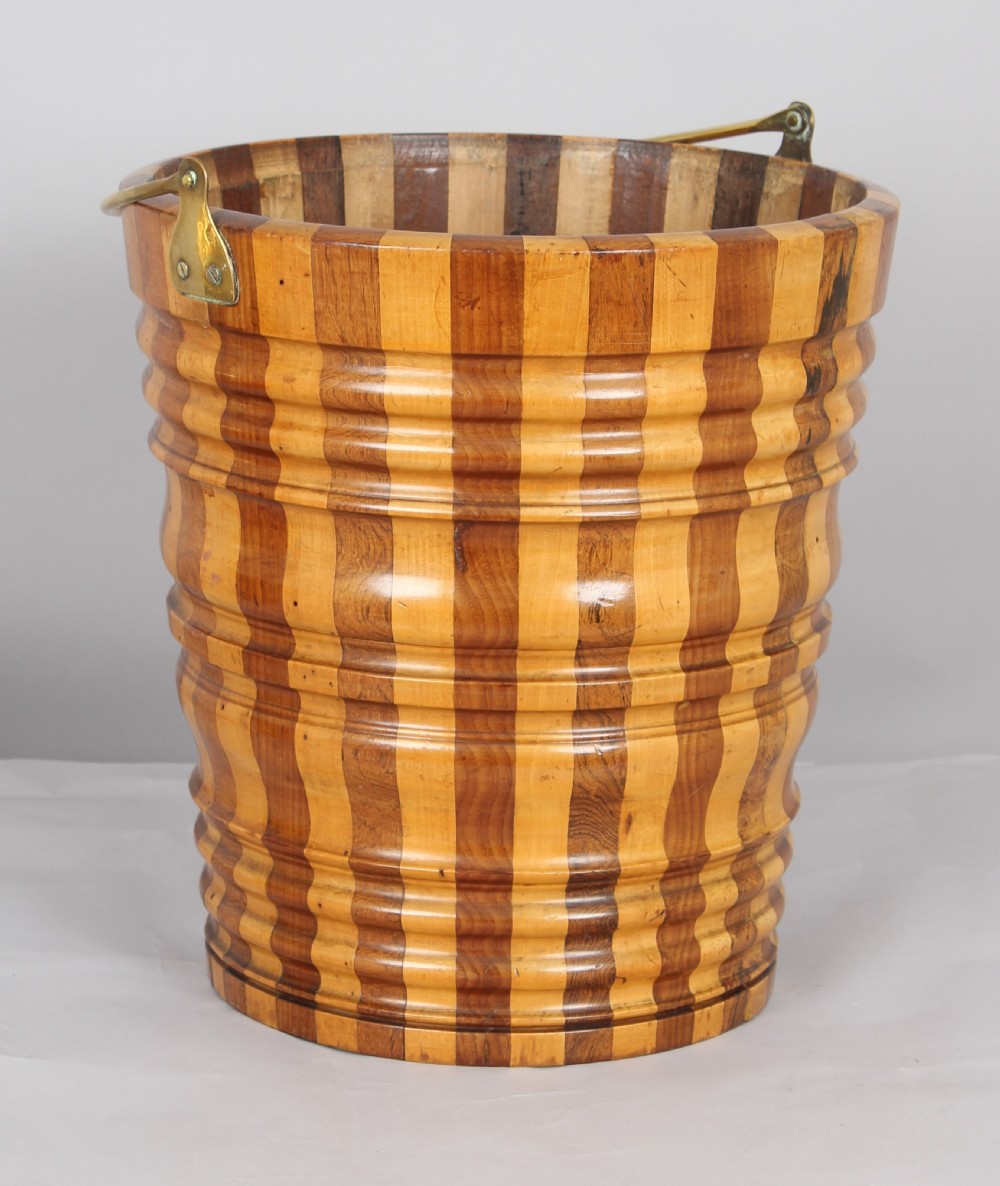 An early nineteenth-century Dutch teestoof bucket featuring alternating light and dark wooden staves, ribbed horizontal shaping, and a brass swing handle.
