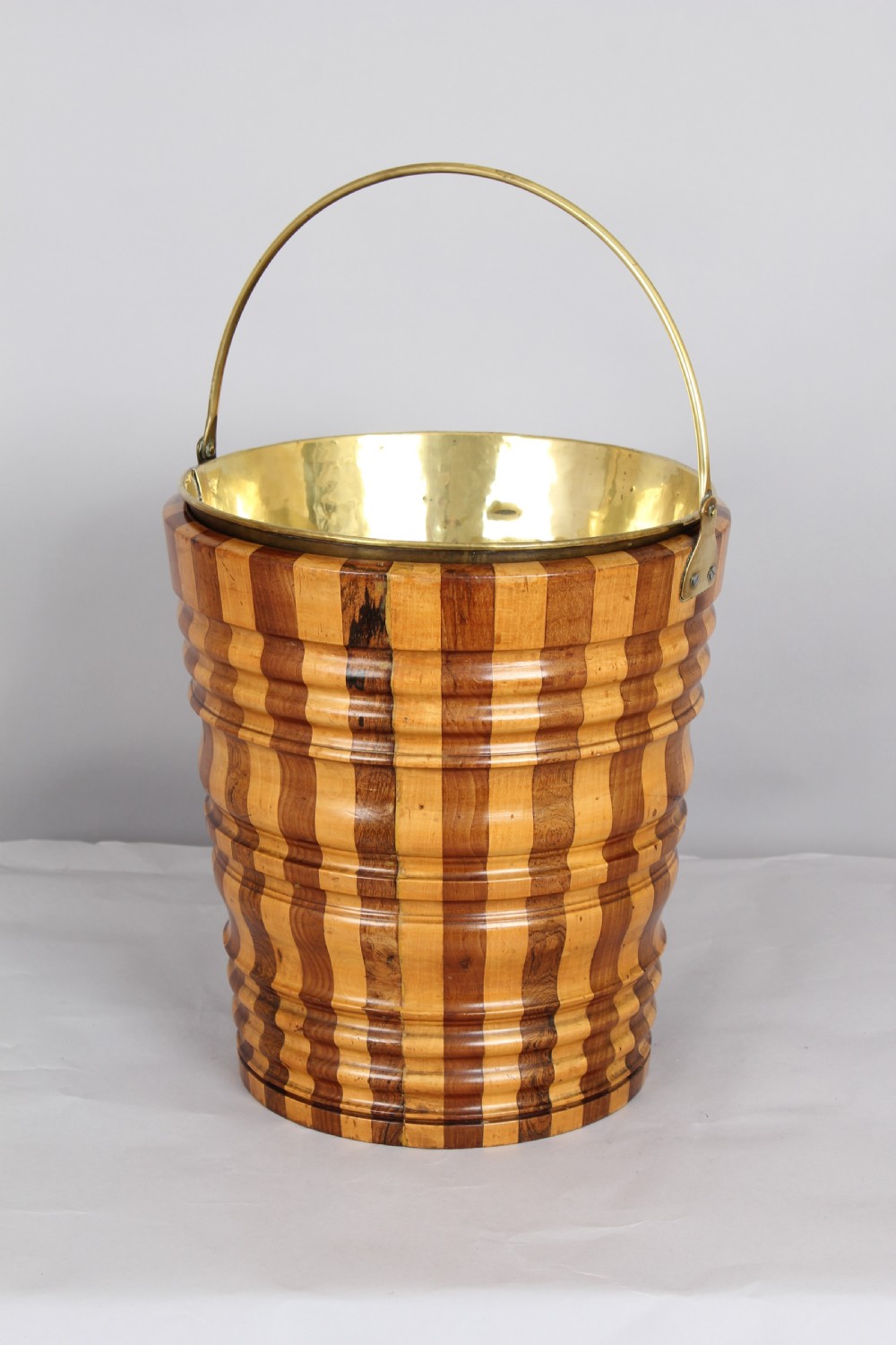 An early nineteenth-century Dutch teestoof bucket featuring alternating light and dark wooden staves, ribbed horizontal shaping, and a brass swing handle. View IV