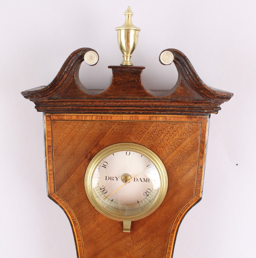A George IV mahogany wheel barometer featuring silvered dials, an integrated clock, thermometer, and brass bezel details. View II