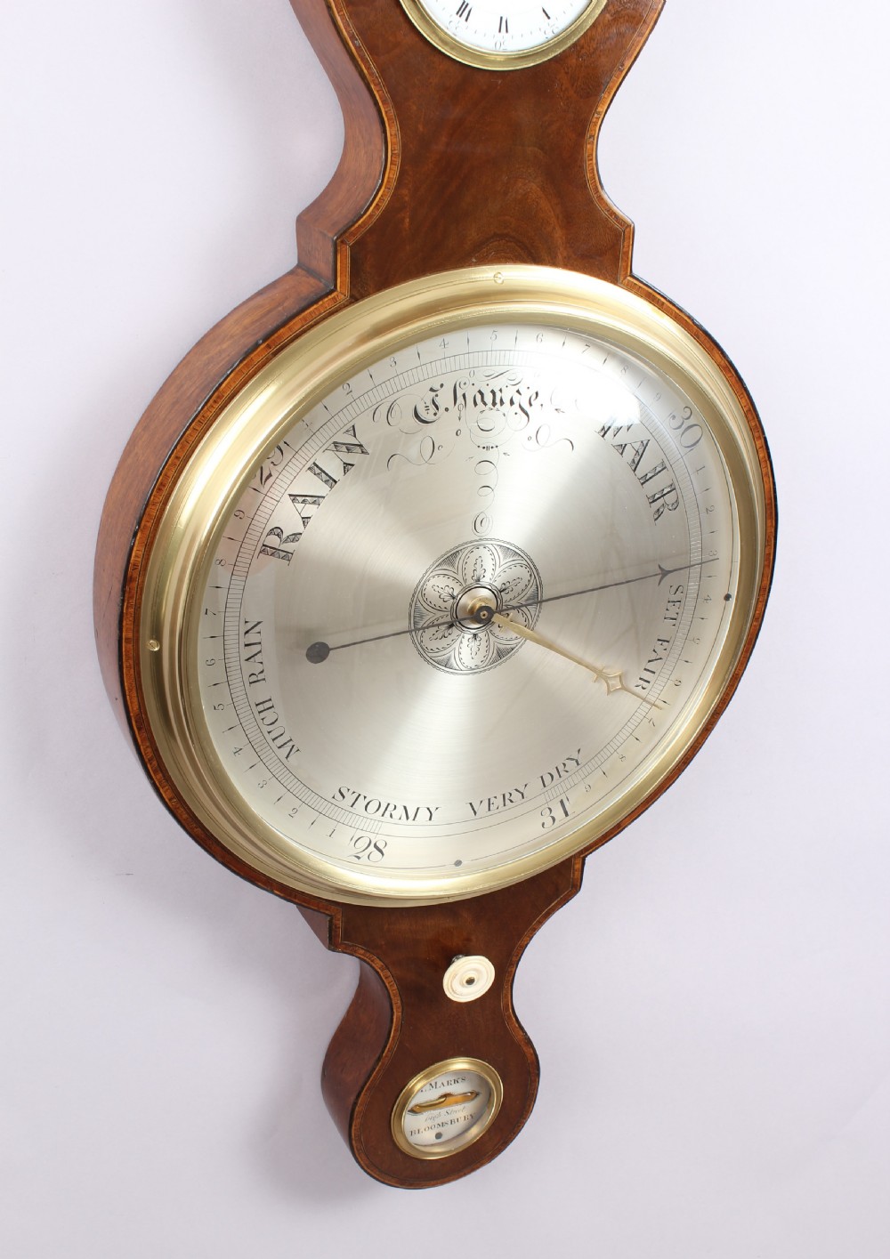 A George IV mahogany wheel barometer featuring silvered dials, an integrated clock, thermometer, and brass bezel details. View IV