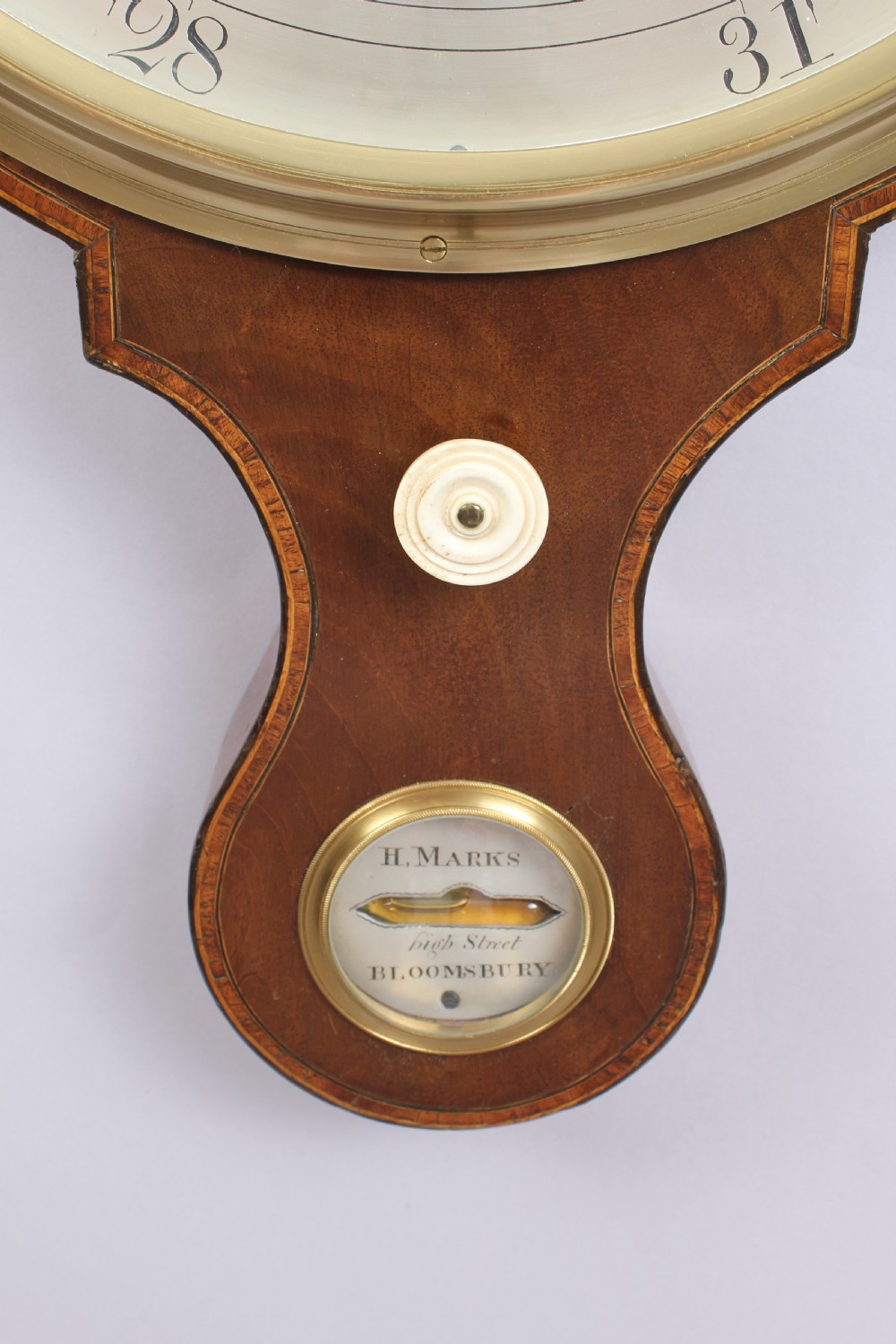 A George IV mahogany wheel barometer featuring silvered dials, an integrated clock, thermometer, and brass bezel details. View V